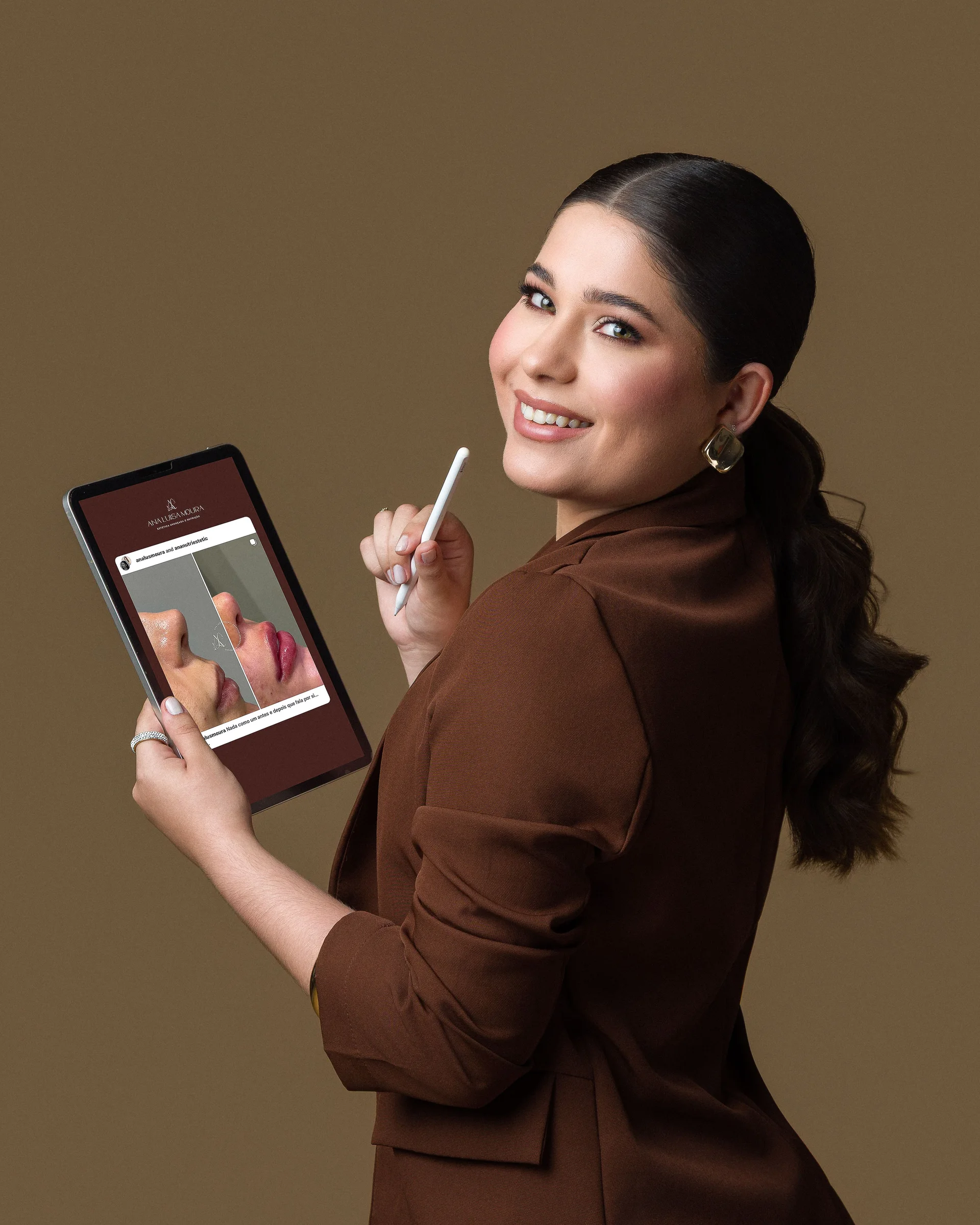 Ana Luisa Moura de terno chocolate, olhando para trás, com um tablet e uma caneta na mão
