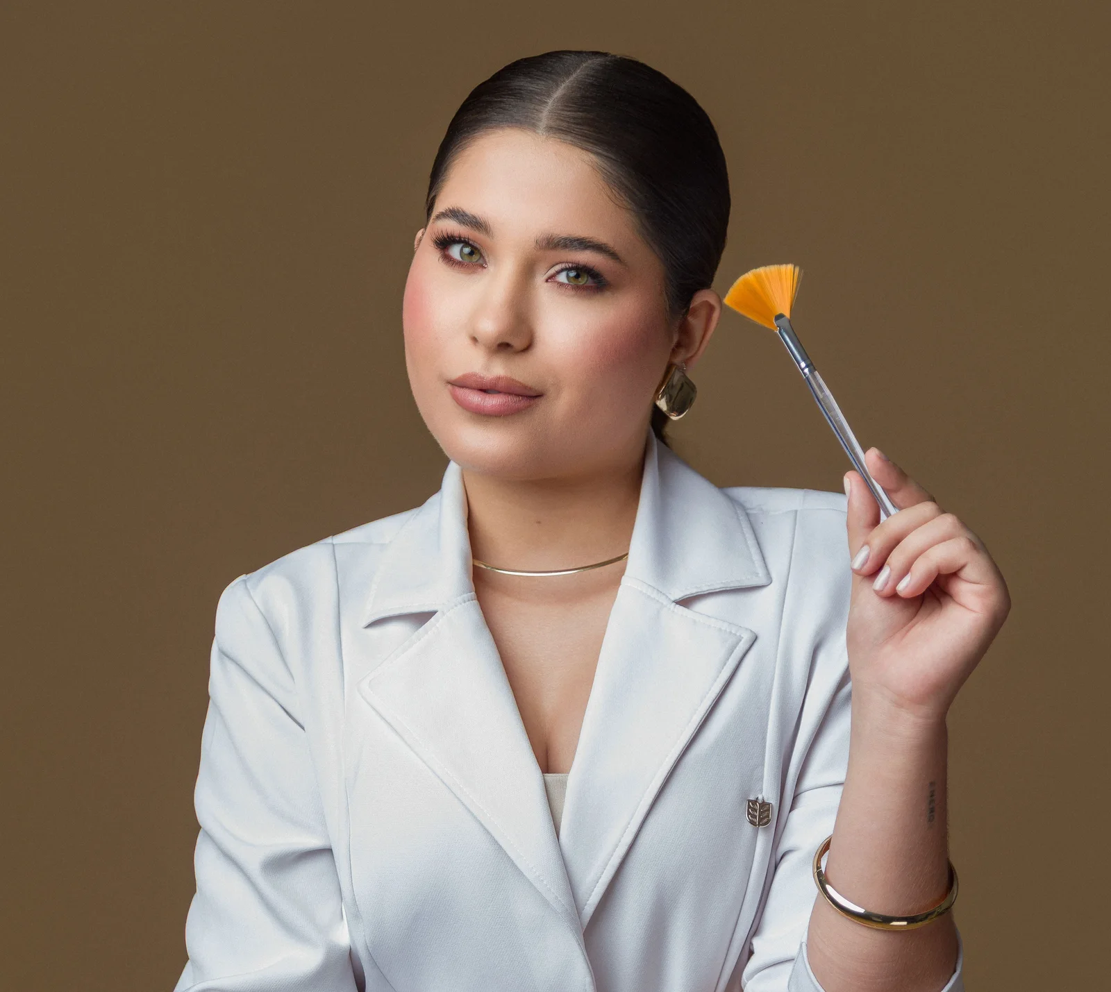 Ana Luisa Moura de blazer branco, segurando um pincel de aplicação de máscara facial